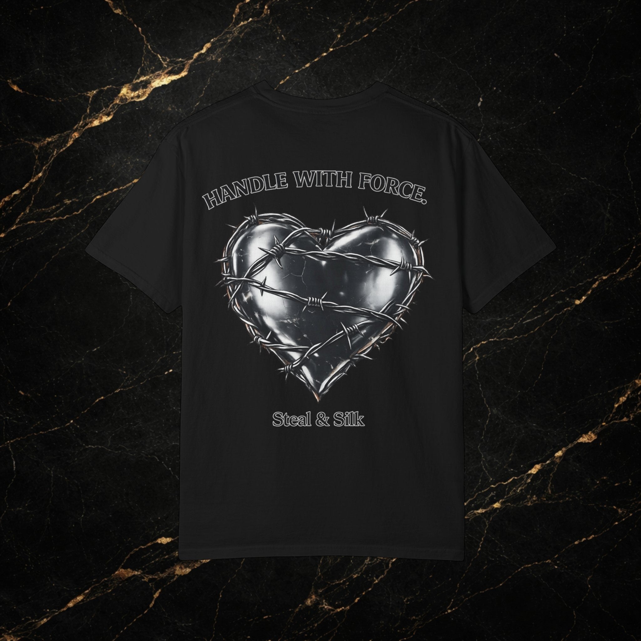 Black cotton t-shirt with a metallic heart graphic wrapped in barbed wire and "Handle With Force" text. Steal & Silk logo below.